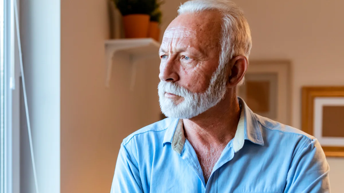 Older man with white beard gazing out window with a concerned expression, reflecting on early warning signs of dementia.