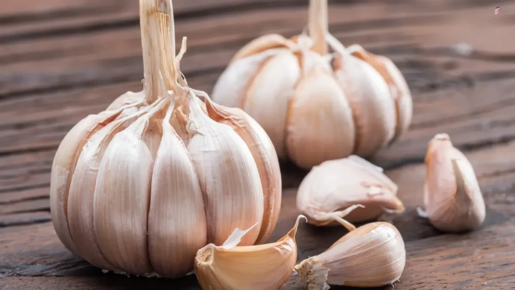Whole garlic bulbs with loose cloves scattered on a rustic wooden table surface
