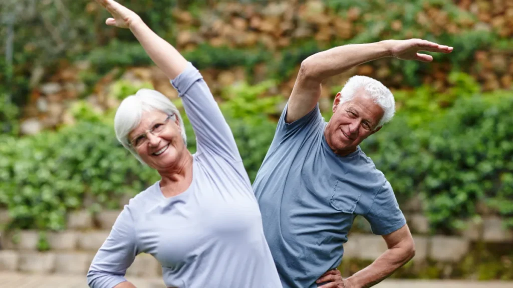 Mature couple performing gentle outdoor stretches during their morning light routine.