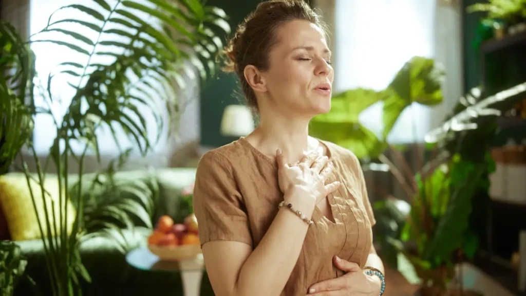 Mature woman breathing deeply with hand on chest to regulate nervous system and support heart rate variability.