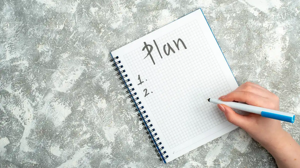 Hand writing a weekly fitness plan in a notebook, representing a structured four week beginner rucking schedule and reset program.