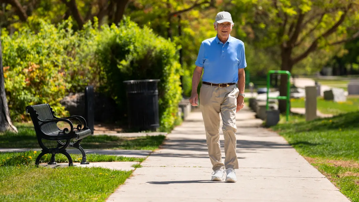 Senior man walking outdoors in a sunny green park, enjoying the mood boosting mental health benefits of outdoor exercise over the gym.