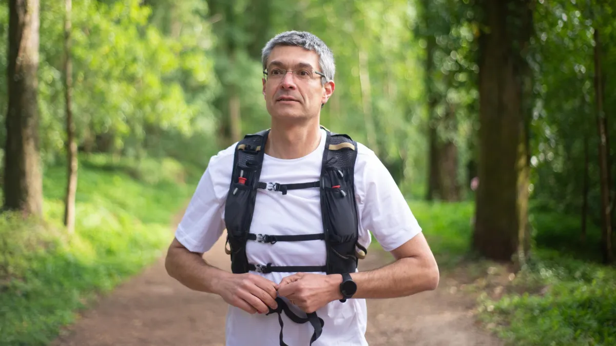 iddle aged man rucking on forest trail with chest and sternum straps properly fastened, demonstrating correct backpack posture for back health.