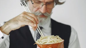 A senior eating pasta with a fork.