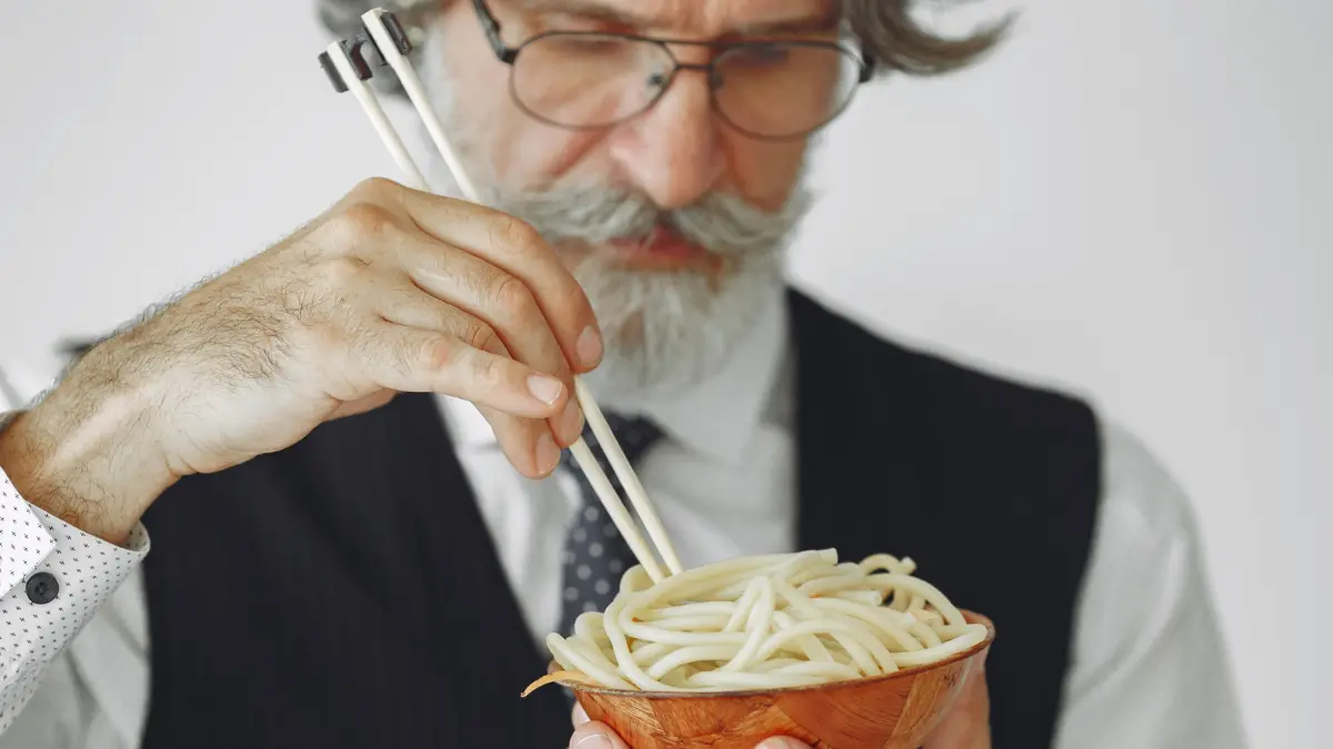 A senior eating pasta with a fork.