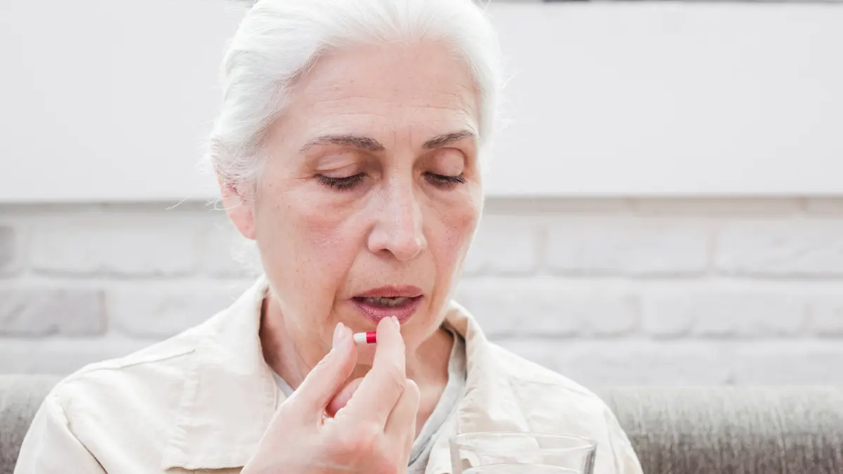 Women over 50 taking a supplement capsule with water, showing medical help for kidney stone prevention