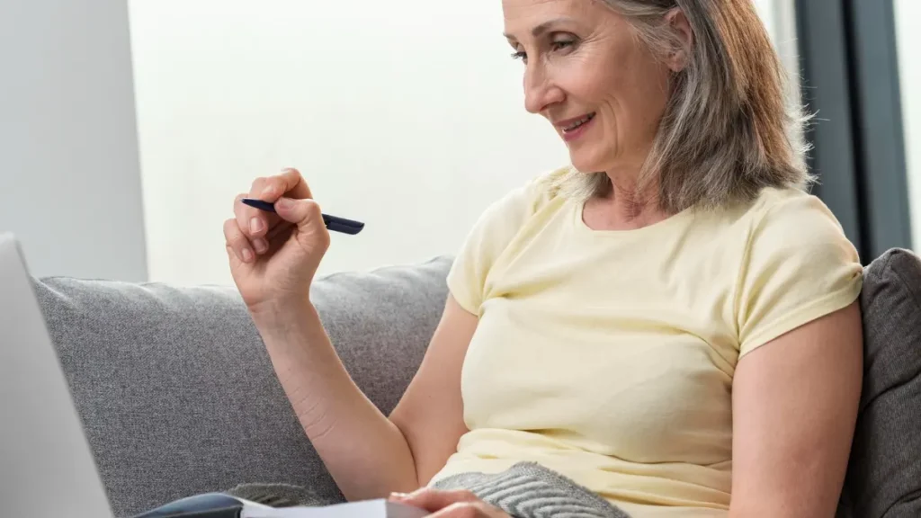 A mature woman uses a laptop to track her seed cycling journey and hormonal health progress over three months.