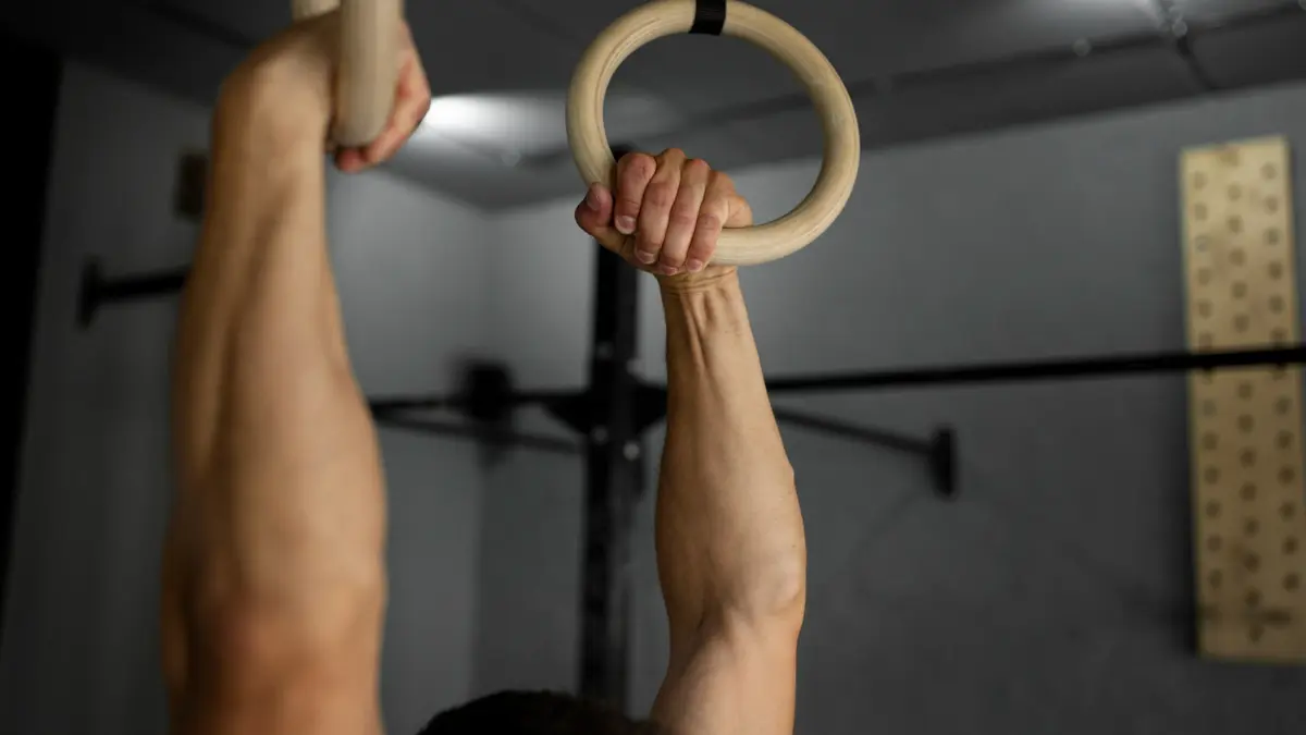 Person hanging from wooden gymnastic rings in a home gym, demonstrating a grip strength hang exercise.
