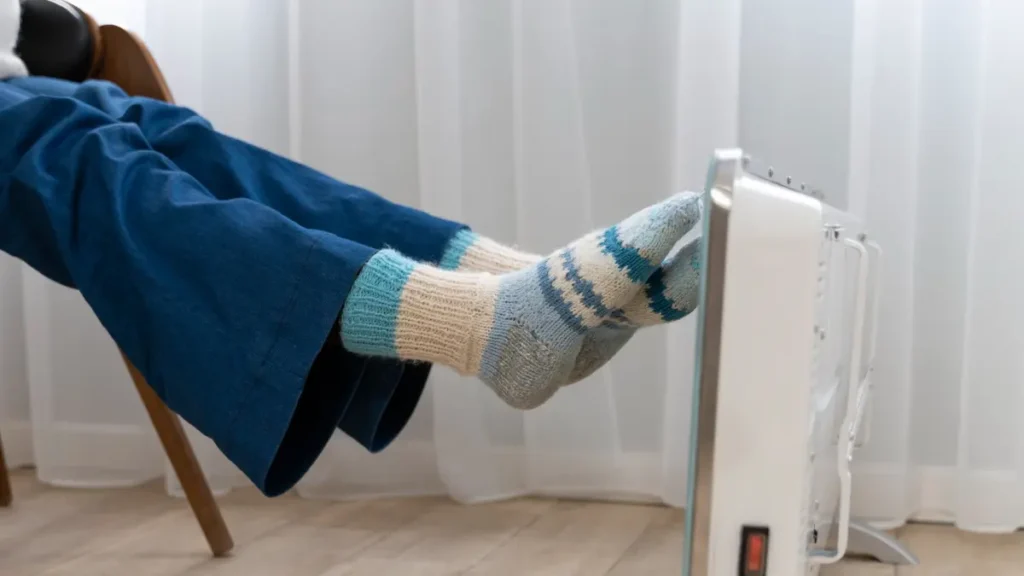 "Feet in thick socks warming against an electric heater to manage cold intolerance from hypothyroidism after 50.