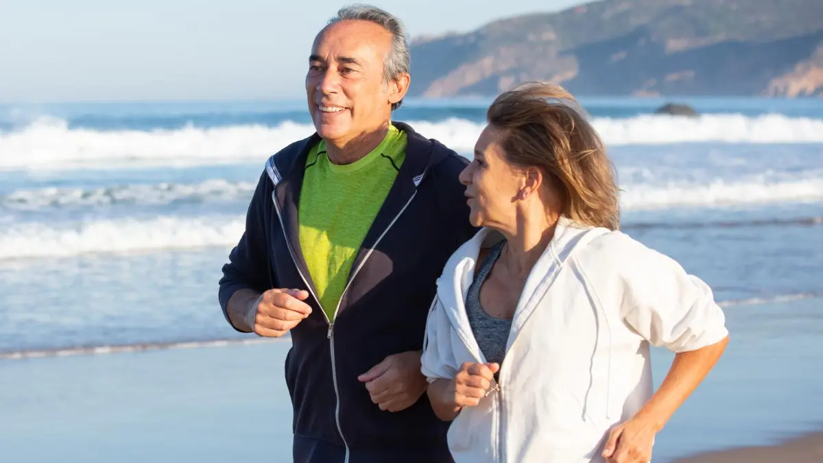 A mature couple walks briskly outdoors while maintaining a conversation to improve stamina after 50