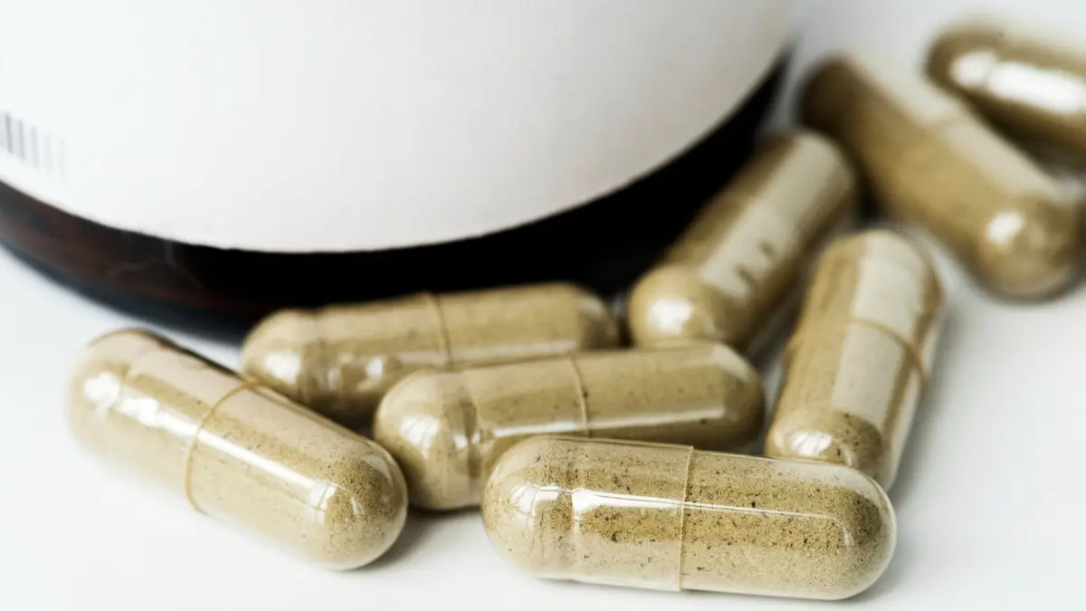 Brown powder filled beef liver supplement capsules spilling from amber bottle for seniors seeking clean grass fed organ supplements.