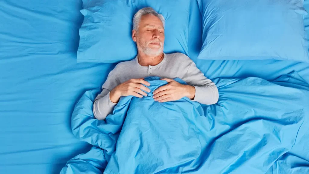 A man in his 60s sleeps deeply in a cool bedroom to support heart tissue repair.