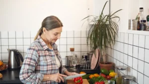 Mature woman examines a red bell pepper in a bright kitchen while preparing a healthy meal
