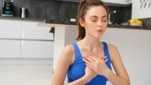 Young woman rubbing her sore neck while sitting in bed in morning light, a sign that belly breathing isn't working.