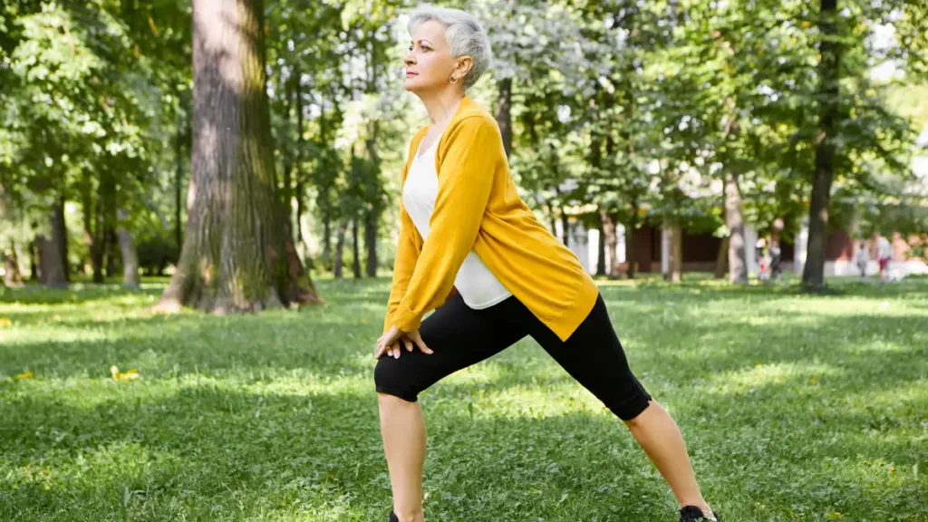 Vibrant elderly woman performs lunges in a sunny park at 9 AM, strengthening joints to ease post-50 bone aches.