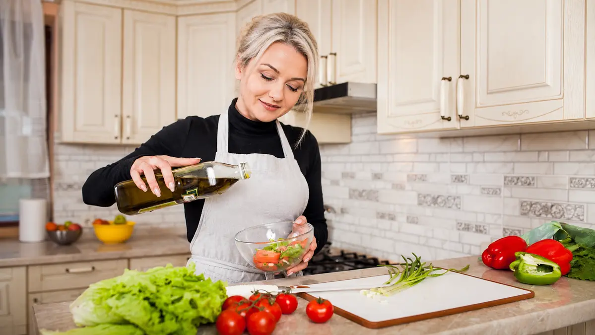 Woman preparing a healthy salad with olive oil and vegetables, supporting brain health, memory, and healthy aging.