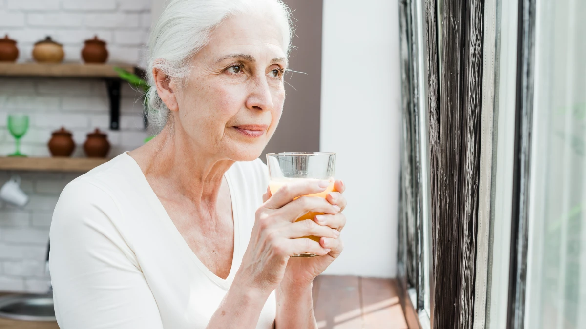 A white-haired senior woman holding a glass of morning smoothie mixed with collagen powder to maintain collagen consistency in the skin.