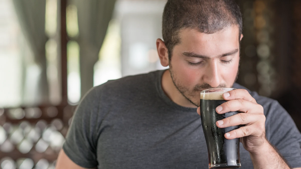 Man drinking dark soda from a tall glass at midday, a fizzy habit that can weaken his bone structure over time.