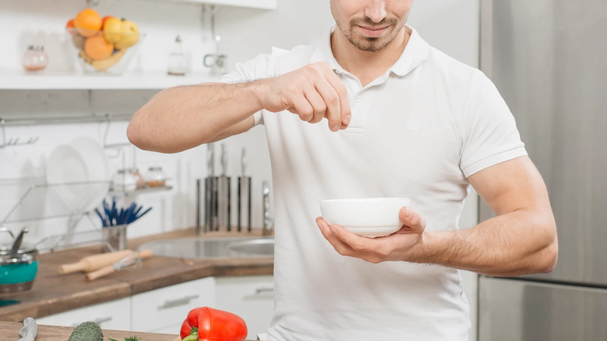 Man sprinkling salt over a steaming pan in his kitchen at noon, excessive salt intake causes calcium loss