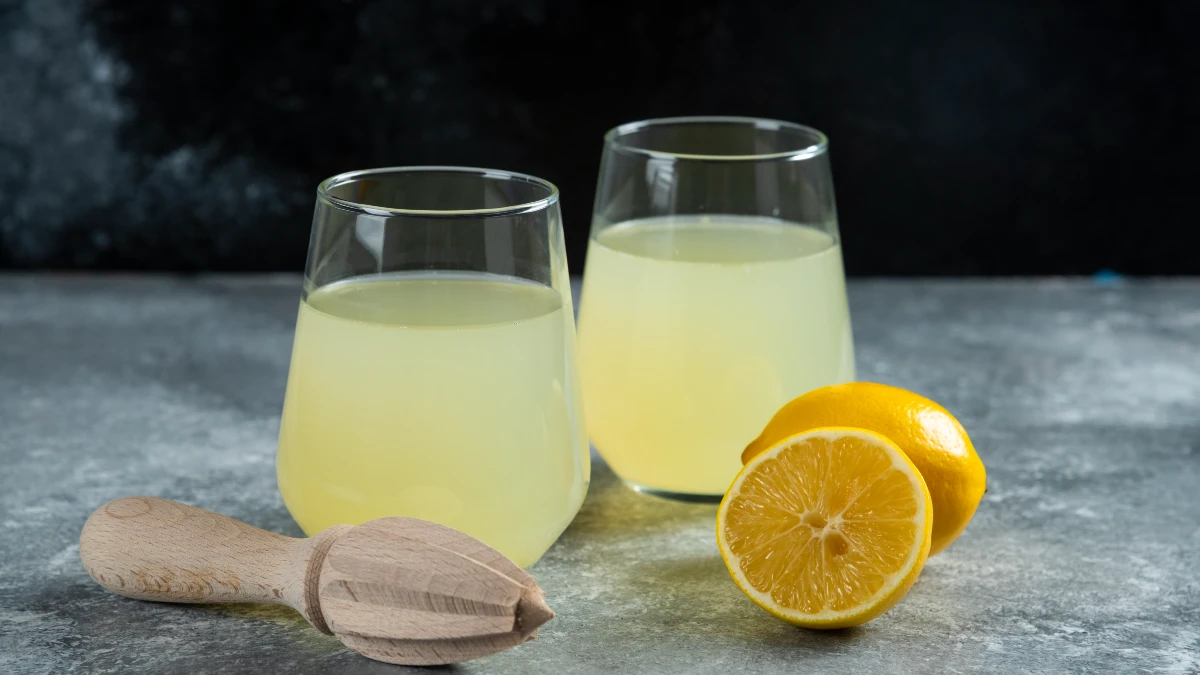 Fresh lemon water in glasses with wooden reamer and sliced lemons, citrate-rich drink to prevent stones 