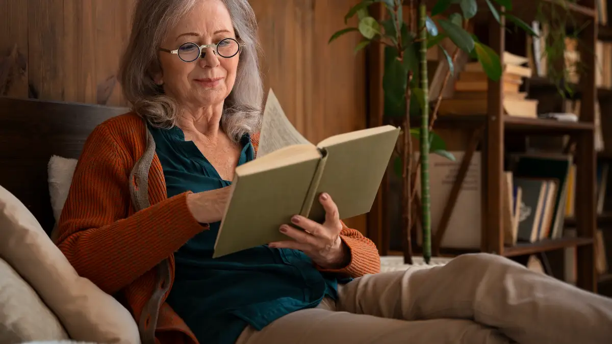 Mature woman reads a physical book in a dark bedroom to lower cortisol at night for better sleep