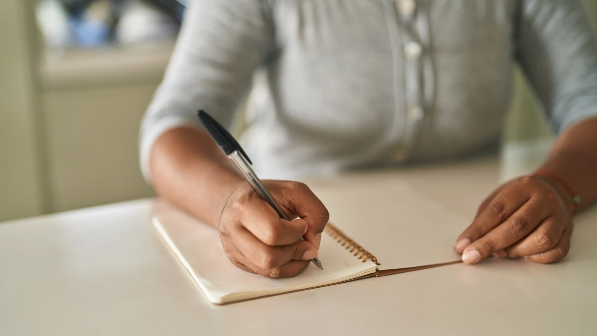 Hands of a woman over 50 writing a brain dump list to manage hormonal balance and mental stress.