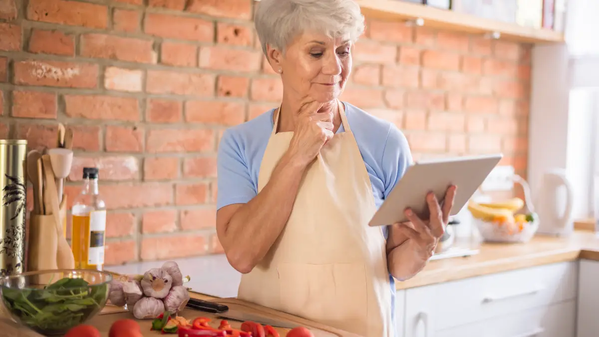 Mature woman in a kitchen, looking at an iPad screen, thinking about lectin-free diets and gut health.