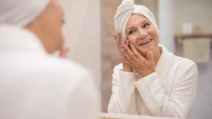 A mature woman examines her skin reflection in a bathroom mirror, contemplating her biological age and cellular health