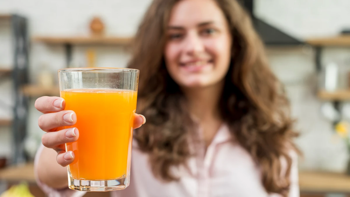 Woman holding glass of low-sugar orange juice, natural citrate source that helps prevent kidney stones
