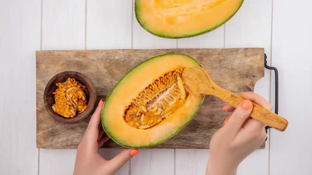 Hand cleaning a fresh pumpkin on a wooden table next to a bowl of seeds, a magnesium source to activate Vitamin D.