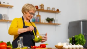 Mature woman in a sunlit kitchen prepares a healthy breakfast to support seed cycling for hormonal balance.