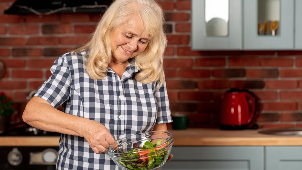 A Blond hair women prepares a fresh salad with broccoli and kale in a sunlit kitchen, focusing on autophagy-boosting foods