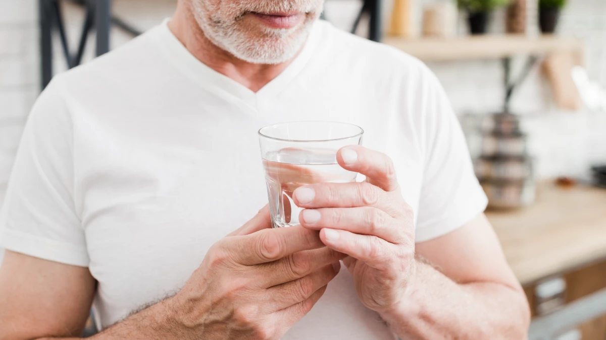A man holding a glass of clear water mixed with sea salt, which replenishes electrolytes during his fasting duration for autophagy