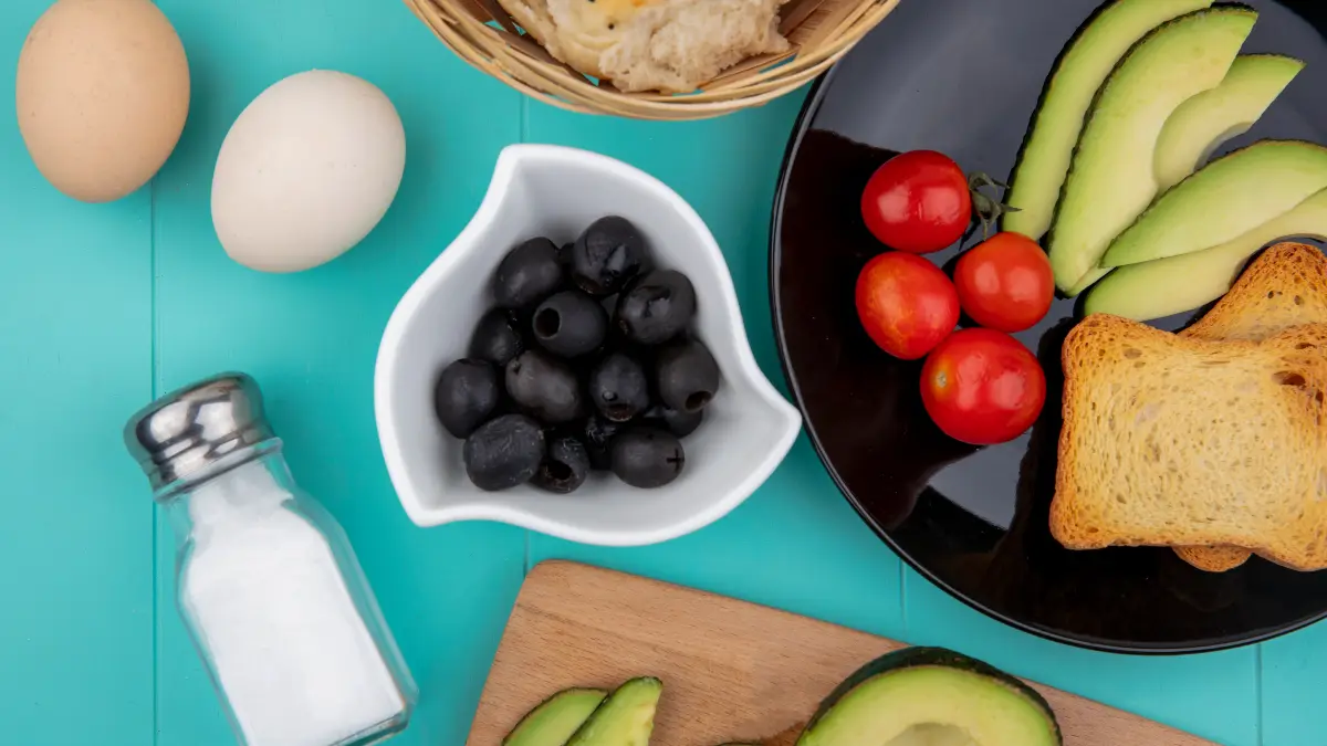 Mediterranean breakfast with avocado eggs olives tomatoes and bread plus salt shaker for sodium potassium balance