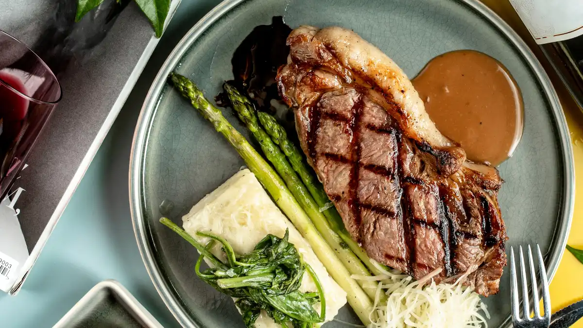 Sliced grass-fed beef steak on a wooden board with grilled asparagus for a high zinc testosterone meal.