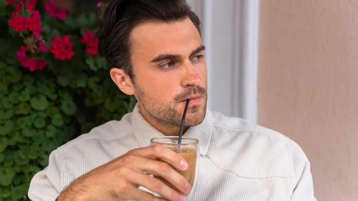Man sipping a cold iced coffee outdoors on a sunny morning break, too much caffeine can limit calcium absorption