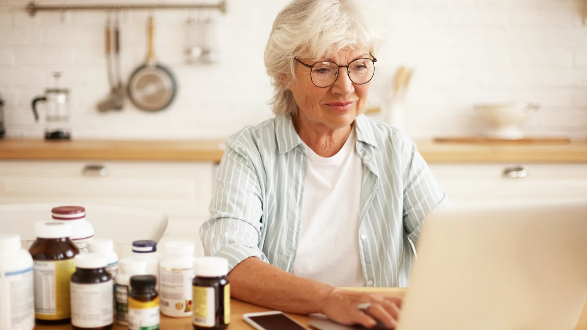 Woman in kitchen reviewing Omega 3 Index Test results on a laptop with supplements placed near her on the counter.