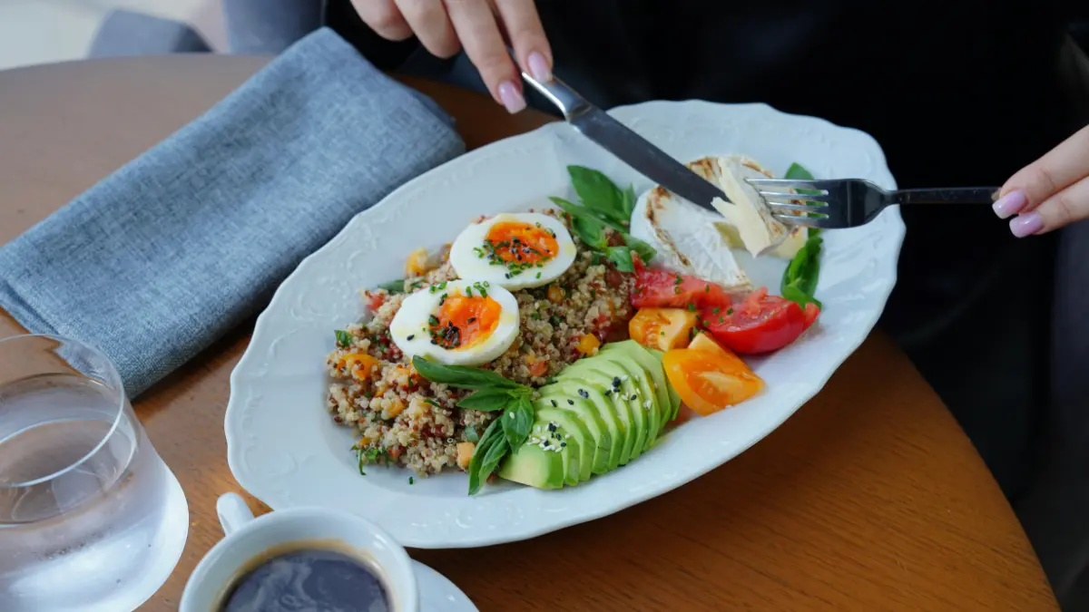 A woman eating a high protein breakfast with eggs quinoa avocado and chicken to support the 7-day perimenopause soft reset plan.