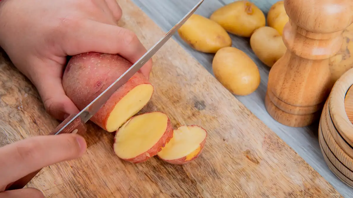 Mature man slicing raw orange sweet potatoes to stabilize blood sugar levels and maintain metabolic heat production