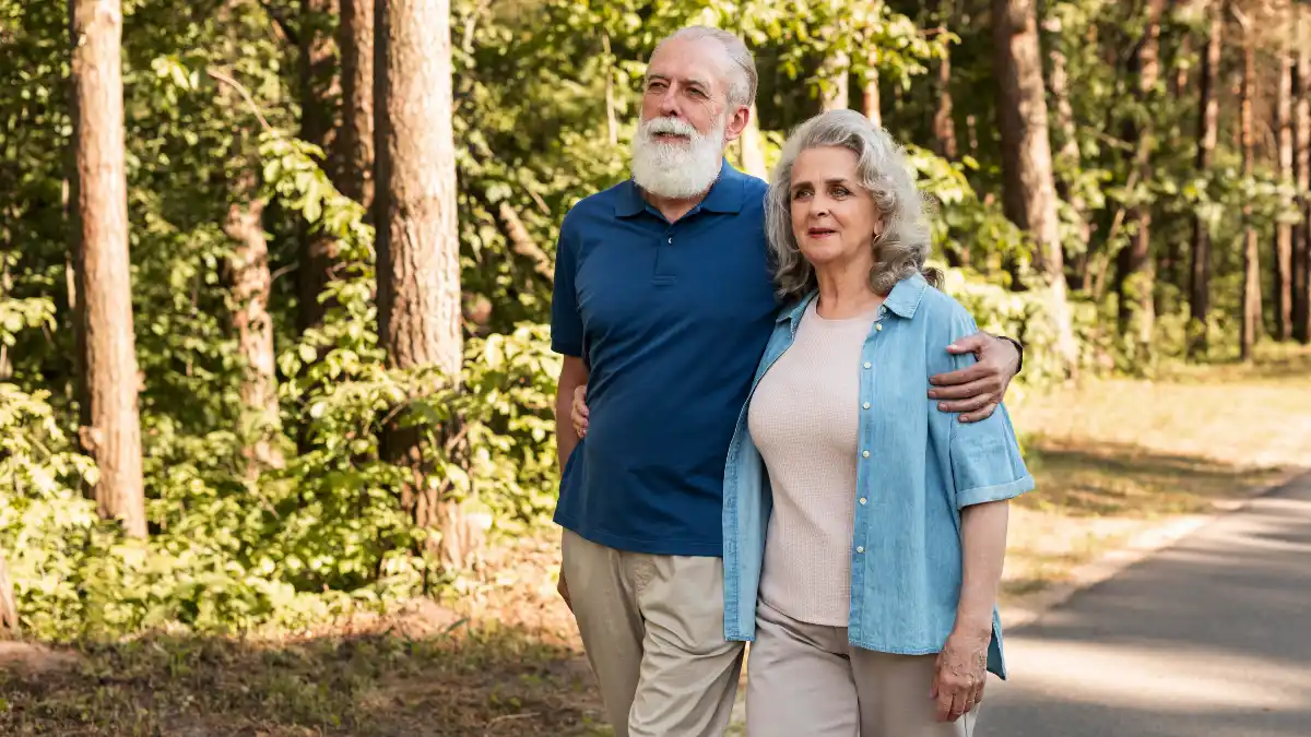 Active couple walking in sunlit park to support joint recovery for elderly mobility and Vitamin D absorption