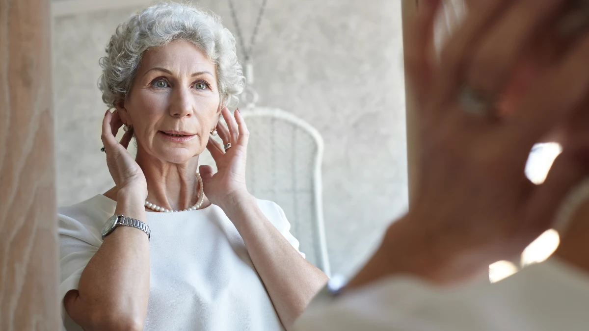 Woman in her 60s inspecting thinning hair in a mirror, a common sign that ferritin levels are low