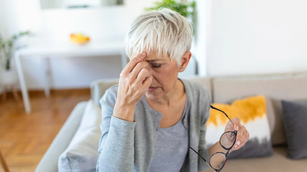 Woman over 50 rubbing tired eyes while holding glasses indoors showing eye strain linked to gut health and digestion problems.