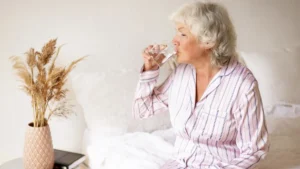 Mature woman drinking water upon waking to support her basal metabolic rate and flush the glymphatic system after deep sleep.