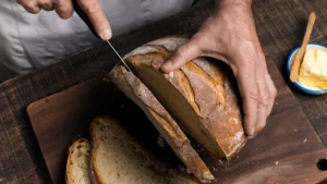 Mature hands slicing a crusty no-knead bread recipe without a dutch oven to reveal the airy crumb.