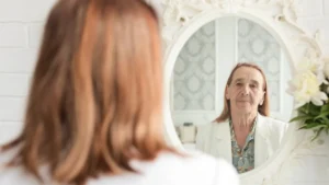 Mature woman looking in a mirror to identify an earlobe crease high blood pressure signal.