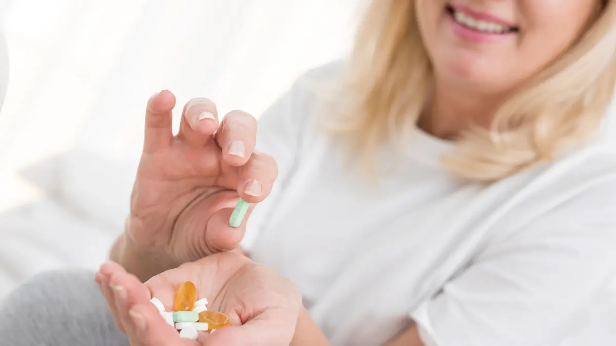 Mature woman smiling while organizing her morning vitamins to optimize supplement timing after 50 for improved energy.