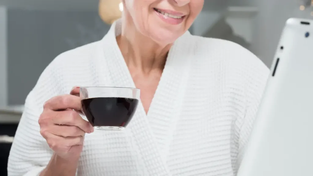 Mature woman drinking black coffee before water, which can lower blood volume and trigger morning dizziness.
