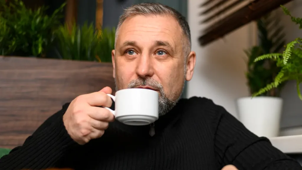 Mature man holding a coffee mug while experiencing high cortisol and a post-meal energy crash.