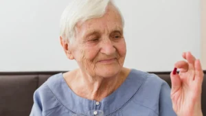 Mature woman holding a calcium capsule and water glass while managing her protocol to avoid calcium without K2 after 50 arterial stiffness.
