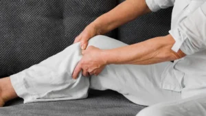 Mature woman gripping her calf to soothe night leg cramps after 50 while resting on a sofa.